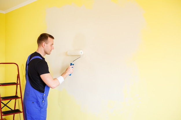 Un uomo dipinge il muro in casa con un rullo e vernice. Ristrutturazione delle stanze della casa.