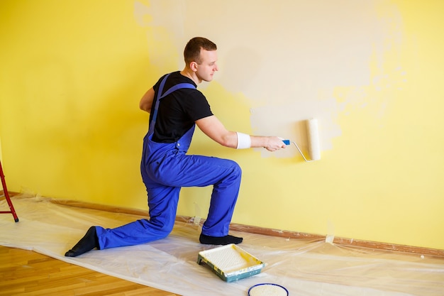 Un uomo dipinge il muro in casa con un rullo e vernice. Ristrutturazione delle stanze della casa.