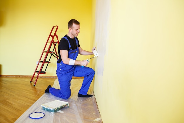 Un uomo dipinge il muro in casa con un rullo e vernice. Ristrutturazione delle stanze della casa.