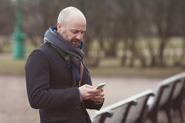 Un uomo è in piedi in strada e aspetta qualcuno Guarda il suo telefono e compone un numero