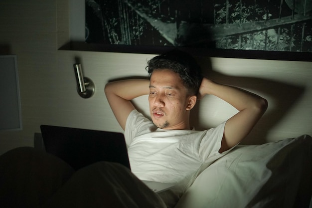 Un uomo è sdraiato a letto con un laptop in mano di notte in hotel