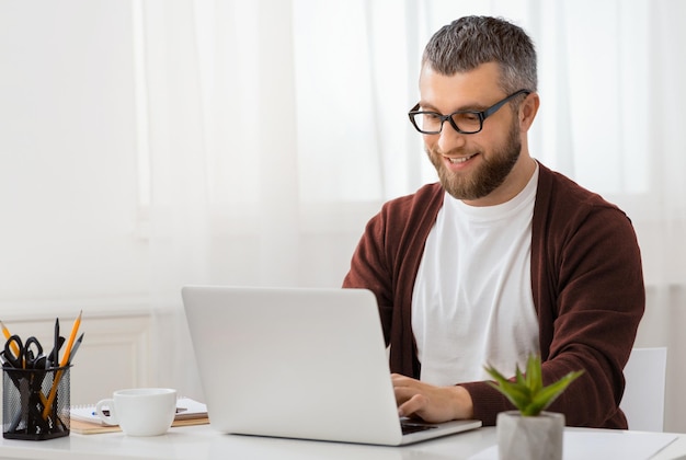 Un uomo è seduto a una scrivania concentrato sullo schermo del suo computer portatile le sue mani stanno digitando sulla tastiera