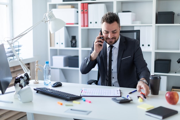 Un uomo è seduto alla scrivania in ufficio, parla al telefono e prende un pennarello in mano