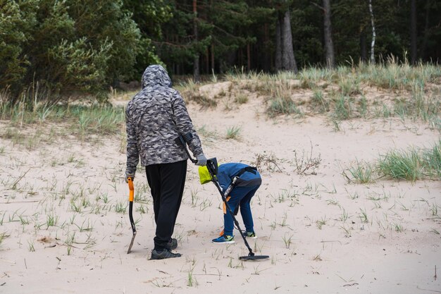 Un uomo e suo figlio cercano un tesoro con il metal detector sulla spiaggia vista da dietro