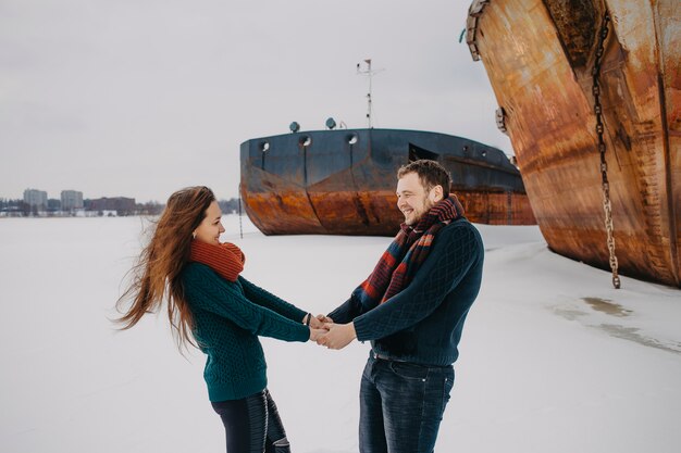 Un uomo e una donna camminano in inverno su un fiume ghiacciato vicino alle navi.