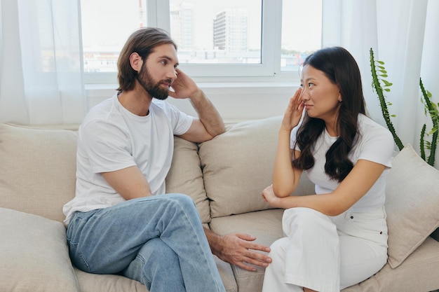 Un uomo e una donna di razze diverse siedono sul divano in una stanza di casa e parlano dei loro problemi tra loro Uno stile di vita senza stress di liti familiari con supporto psicologico