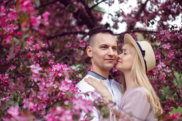 Un uomo e una donna in cappello in ritratto stanno accanto a un ciliegio rosa in fiore in estate