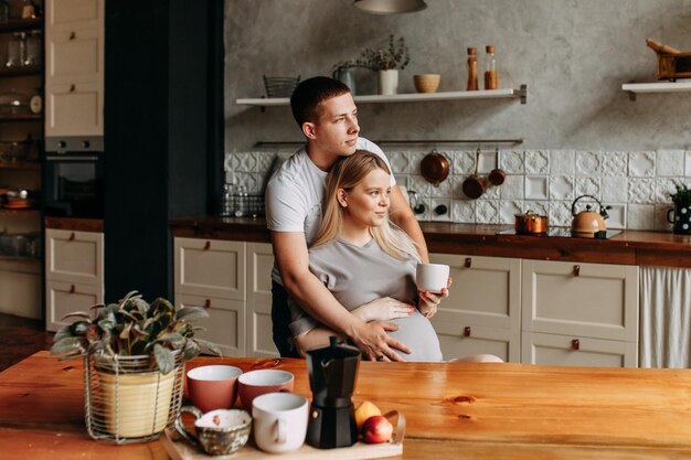 Un uomo e una donna incinta innamorati si abbracciano in cucina e fanno colazione a casa