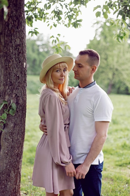 Un uomo e una donna innamorati con un vestito e un cappello sono in piedi su un campo verde sotto un albero in estate