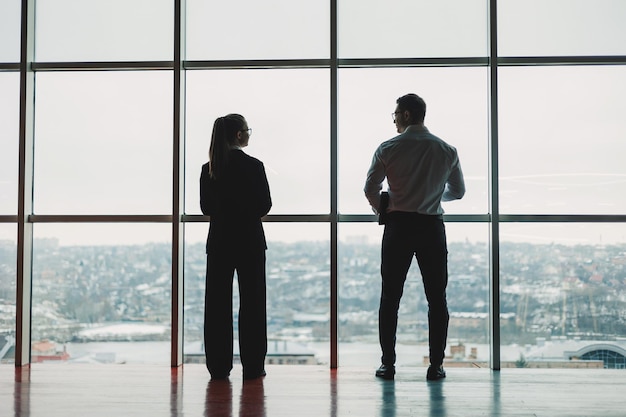 Un uomo e una donna sono in piedi in ufficio sullo sfondo di una grande finestra panoramica moderno spazio di lavoro spazioso con dipendenti partner commerciali