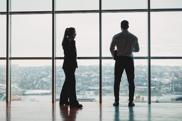 Un uomo e una donna sono in piedi in ufficio sullo sfondo di una grande finestra panoramica moderno spazio di lavoro spazioso con dipendenti partner commerciali