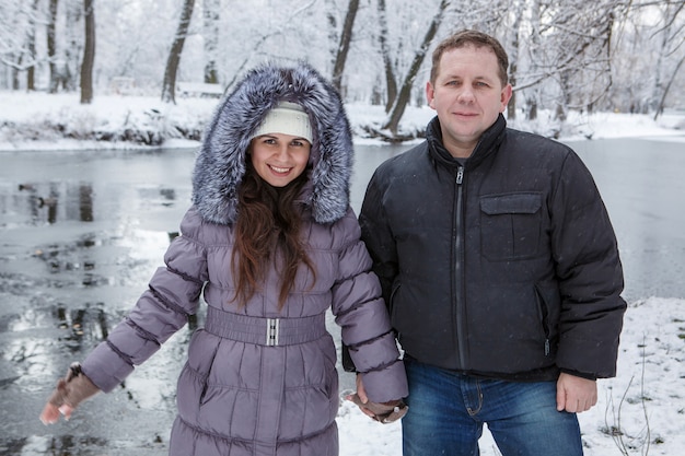 Un uomo e una donna sono in piedi vicino al fiume nel parco innevato in giornata invernale