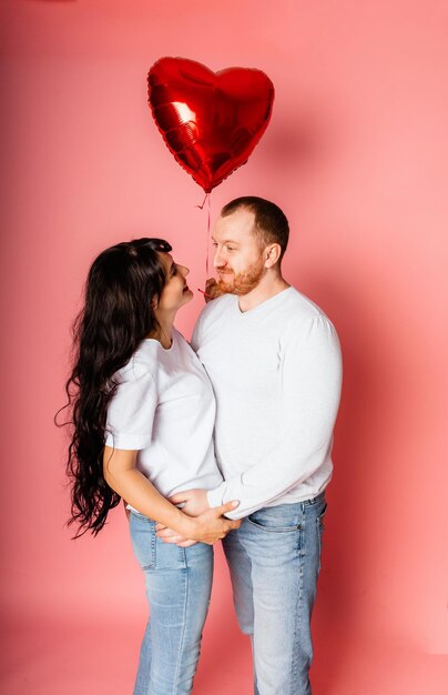 Un uomo e una donna su sfondo rosa tengono in mano un grande pallone gonfiabile rosso a forma di cuore. Concetto di vacanza - San Valentino