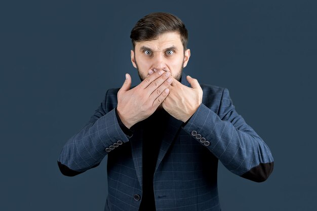 Un uomo elegante con la barba in abito blu si coprì la bocca con due mani