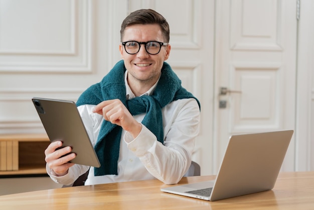 Un uomo elegante con un tablet trasuda fiducia a una scrivania con un laptop e una decorazione classica
