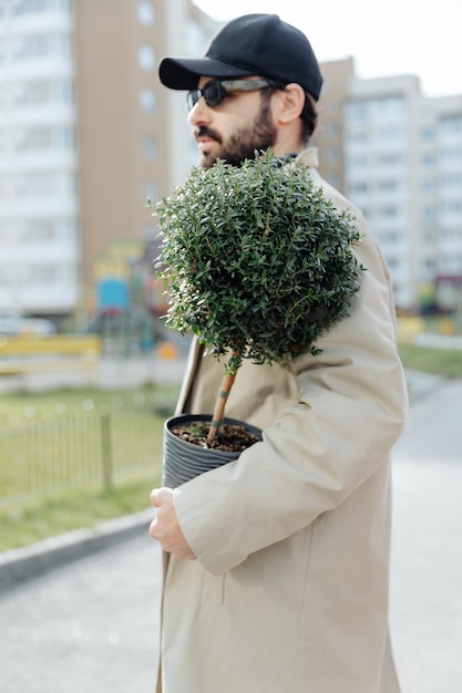 Un uomo elegante con un vaso di fiori in mano sullo sfondo di una casa di nuova costruzione in un quartiere residenziale