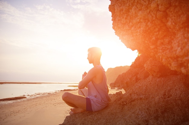 Un uomo fa yoga al tramonto sugli scogli