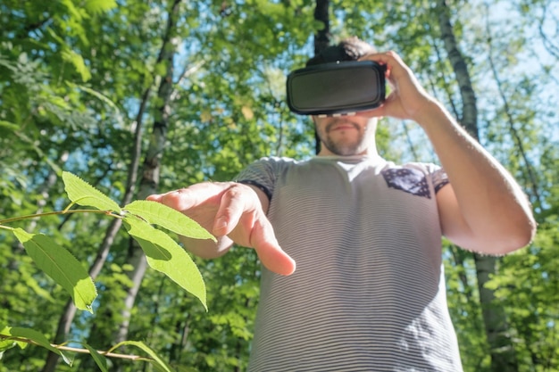 Un uomo felice che fa esperienza utilizzando gli occhiali VRheadset della realtà virtuale nella foresta