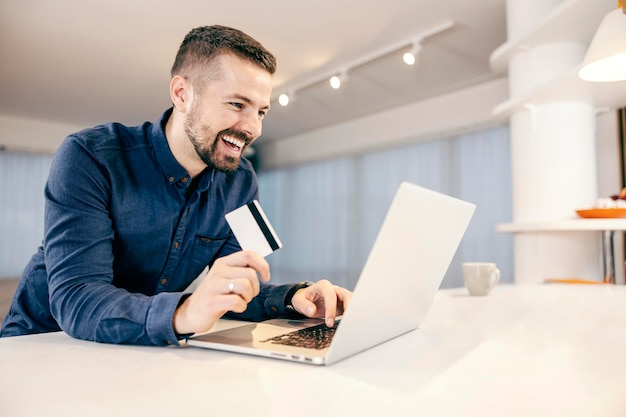 Un uomo felice che prenota lo shopping online e paga le bollette sul laptop dalla sua comoda casa