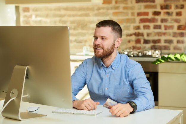 Un uomo felice con la barba aspetta un'asta davanti al computer e tiene in mano una carta di credito