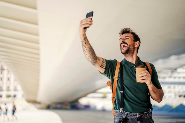 Un uomo felice con un caffè si fa un selfie per strada durante le sue vacanze in Europa