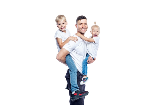 Un uomo felice e bello con dei bambini piccoli tra le braccia un padre con un figlio e una figlia in magliette e jeans sbiaditi amore e tenerezza isolati su uno sfondo bianco