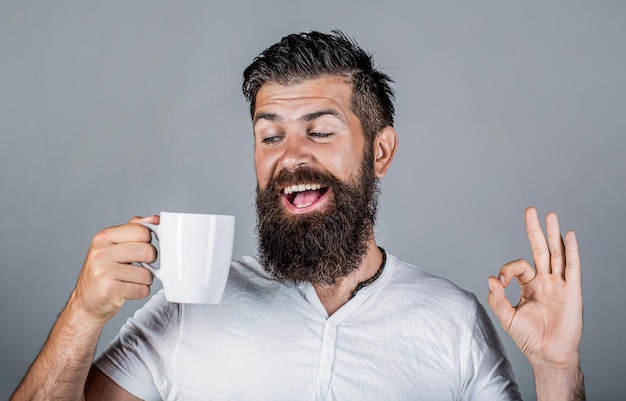 Un uomo felice e sorridente che tiene in mano una tazza di gustoso caffè fresco e mostra il pollice in alto Un uomo tiene in mano la tazza