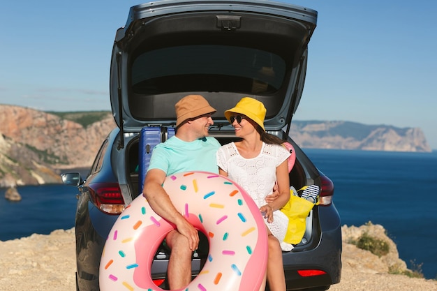 Un uomo felice e una donna sono seduti nel bagagliaio di un'auto vicino al mare