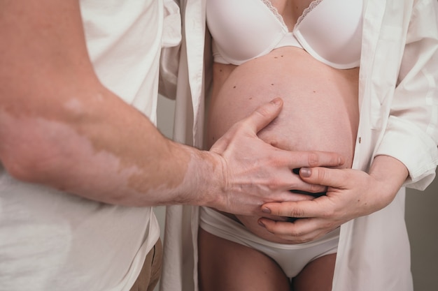 Un uomo felice sta accanto alla sua ragazza incinta. genitori amorevoli stanno aspettando la nascita di un bambino. Il marito abbraccia lo stomaco della moglie incinta.