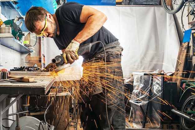 Un uomo forte con mani laboriose in abiti da lavoro che produce una saldatrice per metalli su un tavolo di legno in garage