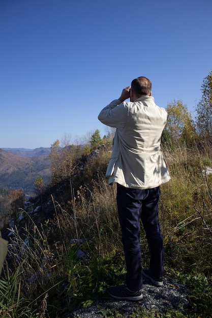 Un uomo guarda attraverso i vetri da campo in piedi sulla cima di una montagna.