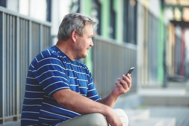 Un uomo guarda sognante in città con in mano uno smartphone e sorride misteriosamente