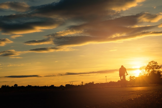 Un uomo guida una bicicletta sulla strada al fondo del cielo al tramonto.