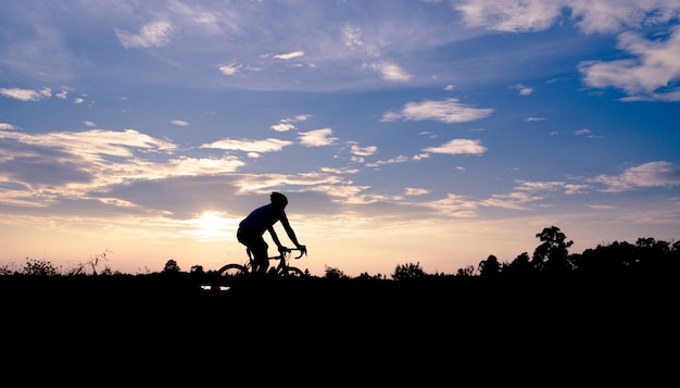 Un uomo guida una bicicletta sulla strada al fondo del cielo al tramonto.