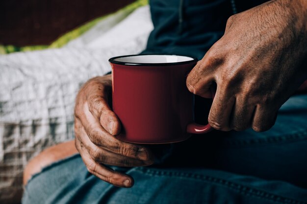 Un uomo implora. Ha in mano una tazza di carta bianca. Il concetto di senzatetto e povertà.