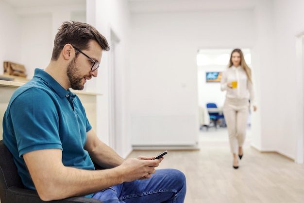 Un uomo in abbigliamento casual è seduto nella sala d'attesa per l'ispezione tecnica e utilizza un telefono