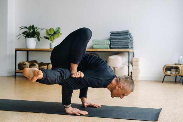 Un uomo in abiti sportivi neri fa yoga in piedi sulle mani che si allungano in palestra