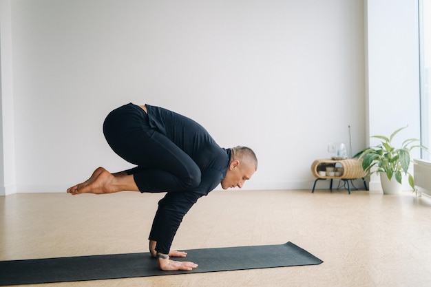 Un uomo in abiti sportivi neri fa yoga in piedi sulle mani che si allungano in palestra