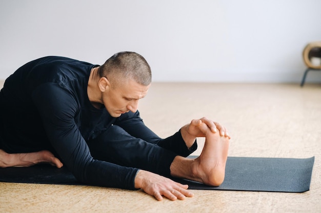 Un uomo in abiti sportivi neri sta facendo stretching Yoga in palestra