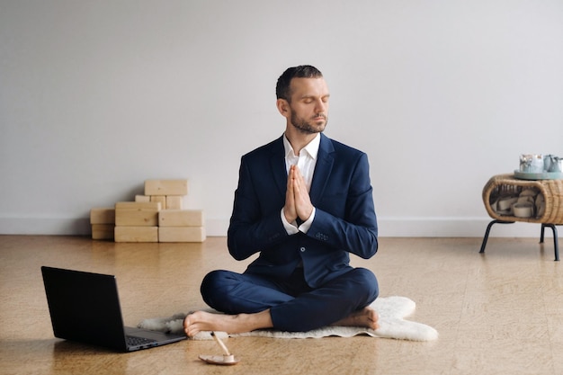 Un uomo in abito formale medita seduto in una sala fitness con un laptop