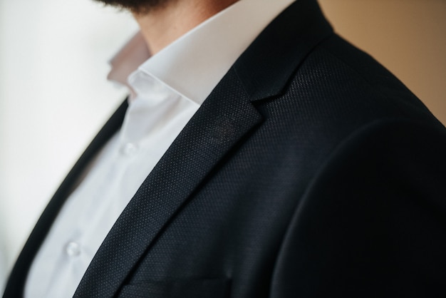 Un uomo in abito nero e camicia bianca posa in casa per pubblicizzare l'abbigliamento maschile. Riprese per negozio di abbigliamento maschile