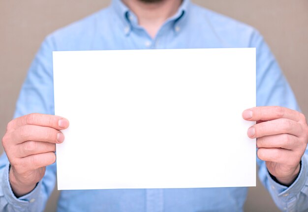 Un uomo in camicia blu, uomo d'affari che tiene foglio bianco bianco. Spazio per testo, mockup