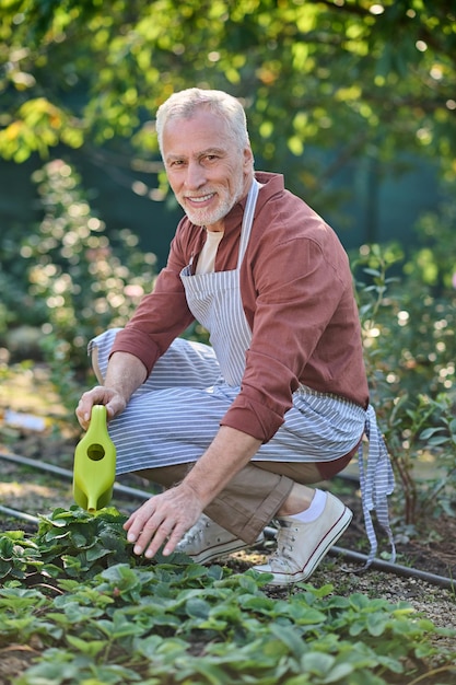 Un uomo in camicia bordeaux che lavora nel suo giardino e sembra occupato