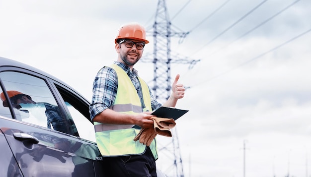 Un uomo in casco e uniforme, un elettricista sul campo. Ingegnere elettricista professionista ispeziona le linee elettriche durante il lavoro.