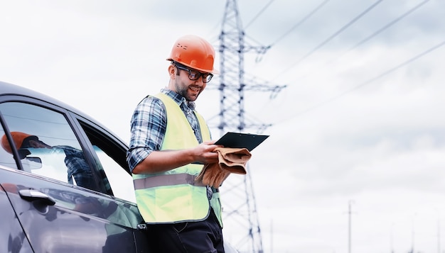 Un uomo in casco e uniforme, un elettricista sul campo. Ingegnere elettricista professionista ispeziona le linee elettriche durante il lavoro.