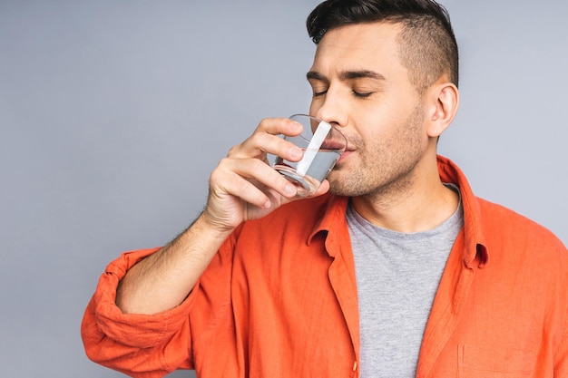 Un uomo in casual isolato su sfondo grigio bianco acqua potabile da un bicchiere