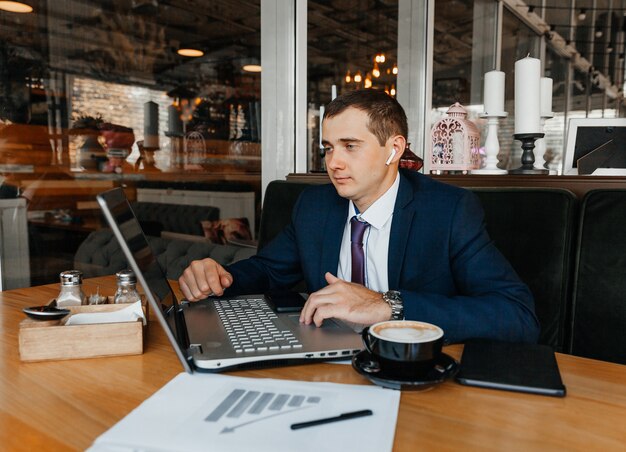 Un uomo in giacca e cravatta lavora su un laptop in un bar. Uomo d'affari con il computer portatile.