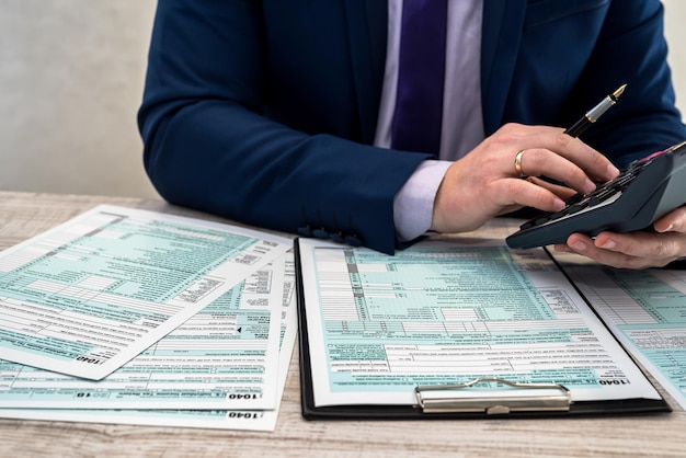 Un uomo in giacca e cravatta scrive un modulo fiscale 1040 in ufficio. Le mani maschili riempiono la carta con la calcolatrice sul posto di lavoro. concetto di contabilità