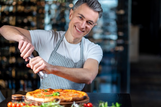 Un uomo in grembiule che prepara pizza vegetariana con pomodorini