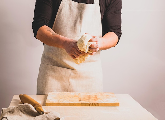 Un uomo in grembiule impasta la pasta fa il pane Il concetto di cottura fatta in casa Messa a fuoco selettiva